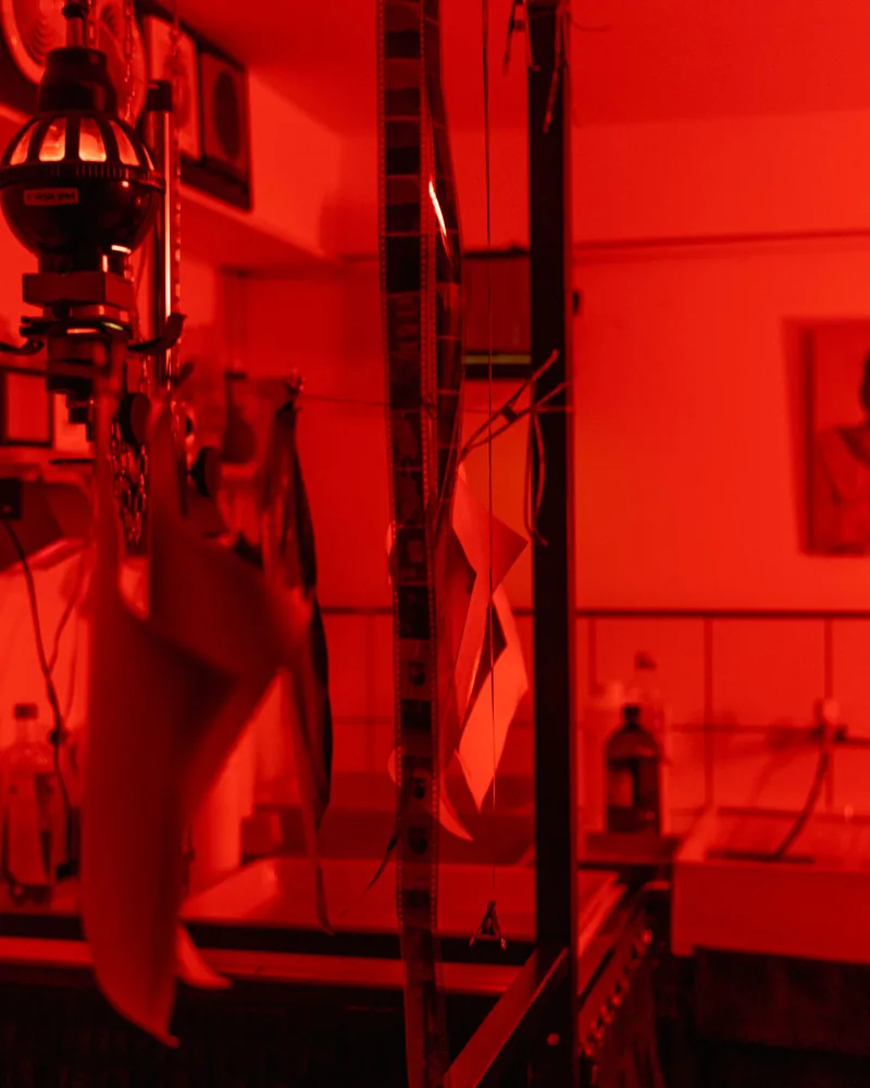 Tiras de negativo colgadas con pinzas para secar en un cuarto oscuro iluminado en rojo